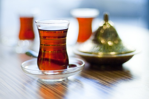Cup of turkish tea served in traditional style with a green pot in the background
